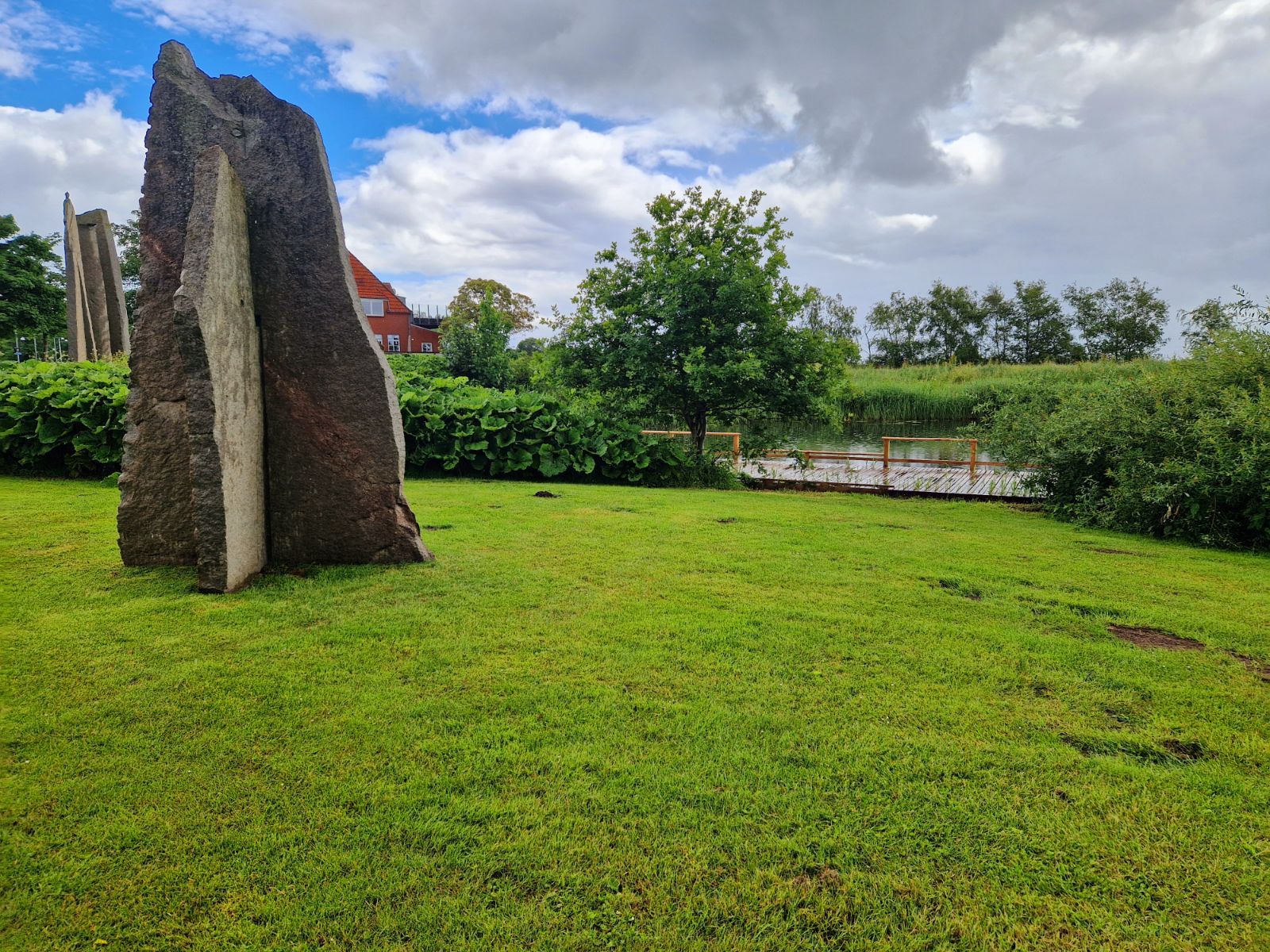 Kig mod stenskulptur og det slåede græsstykke ned mod fiskeplatformen 