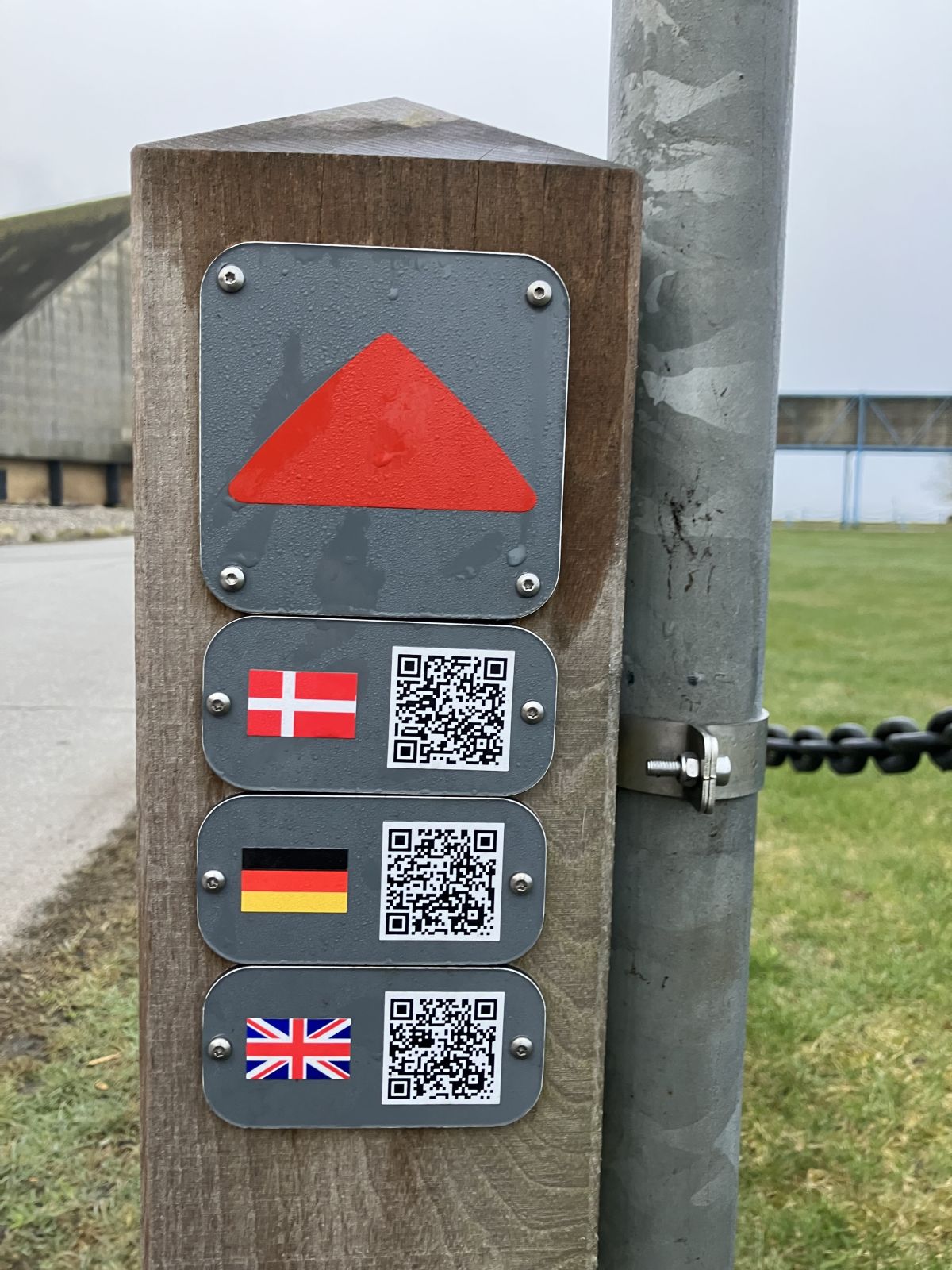 Rutepæl med parkeringstrekanten og QR koder til fortællinger på tre forskellige sprog