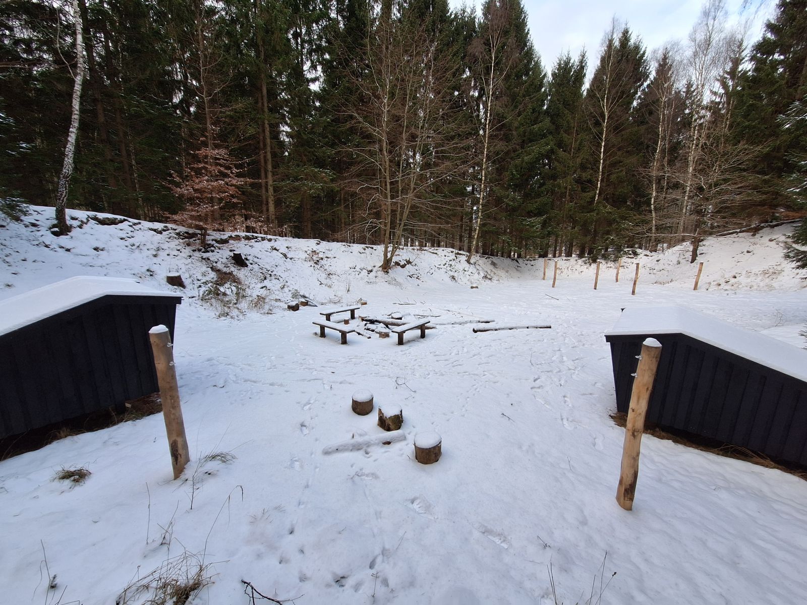Billedet viser to shelters set bagfra. Imellem dem står et sæt 2 m. høje pæle og i baggrunden ses tre lignende sæt pæle.