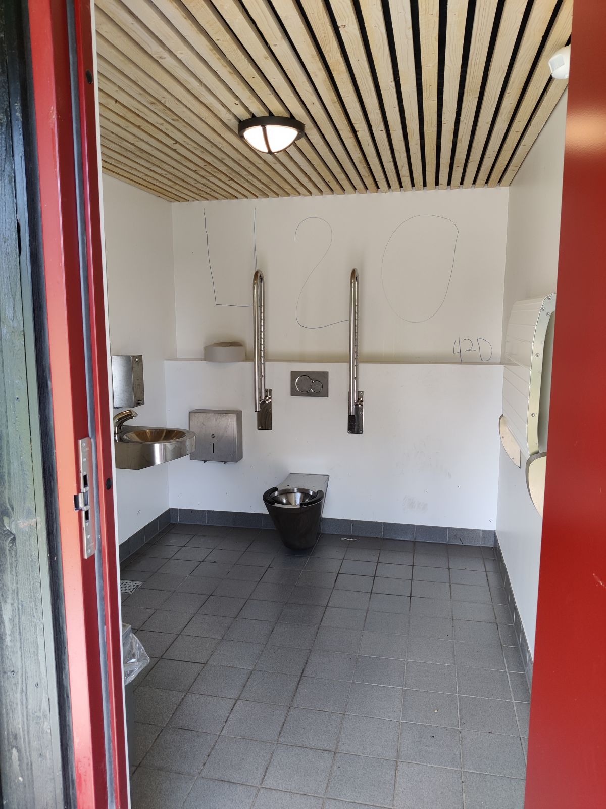 Toilet med armstøtter og wc-papir, pusleplads, håndvask med rindende vand, sæbe og papir.