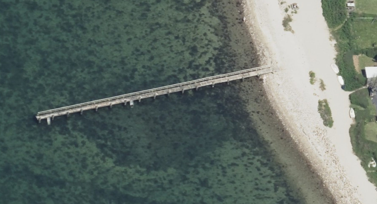 Adgangen til badebroen går over sandstranden. Der er et mindre trin fra stranden til broen.