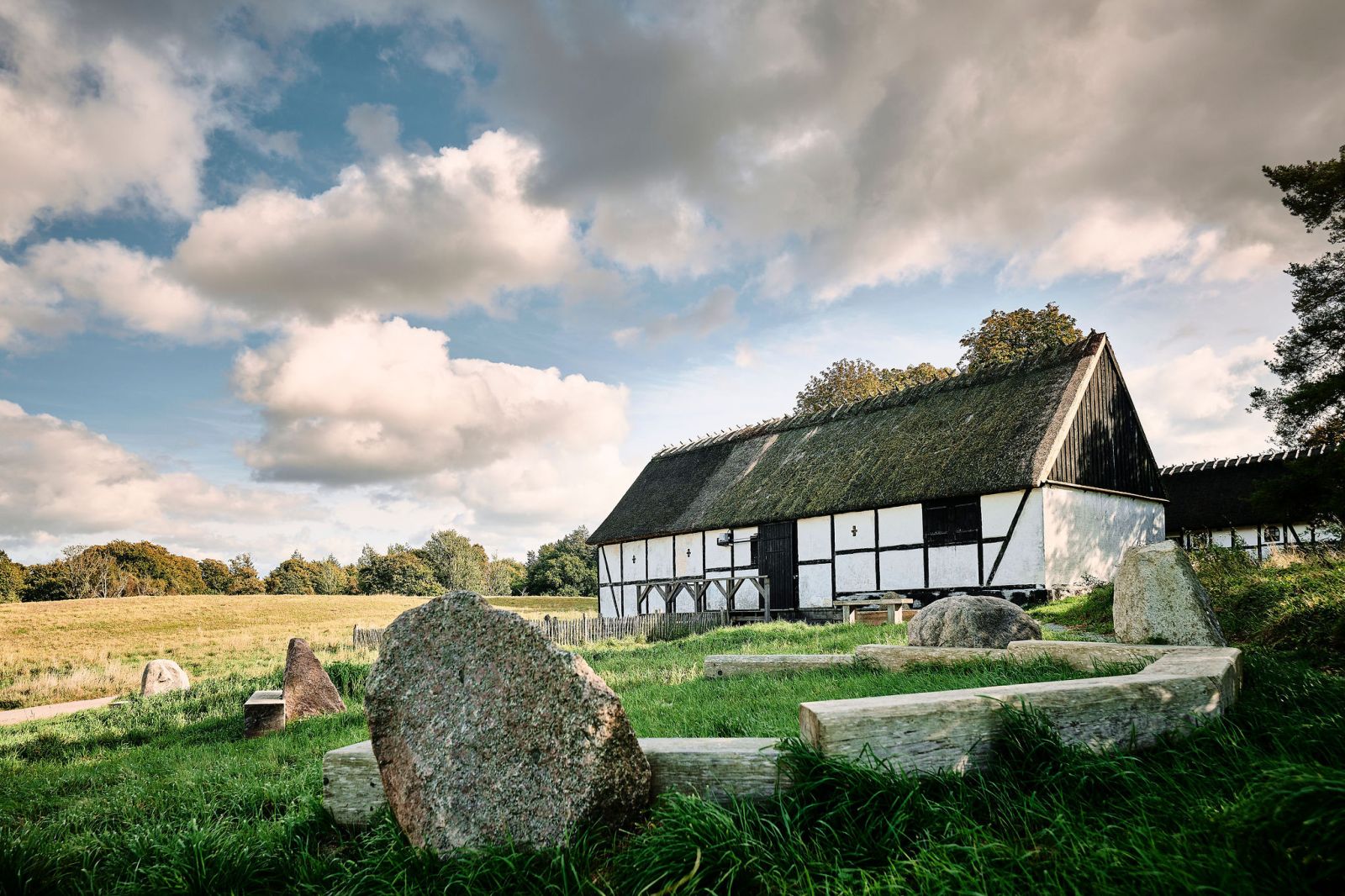 Bygning med bindingsværk og stråtag med bænke forrest i billedet