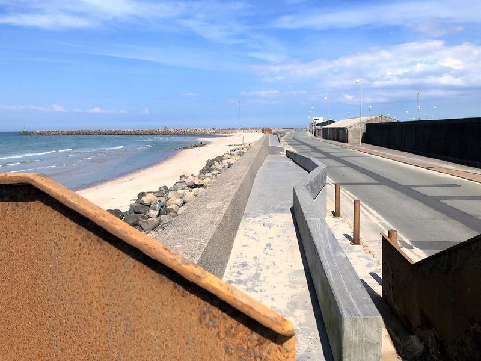 Passage langs Hirtshals havn hvor man kan se havet og stranden til venstre. Underlaget er beton.