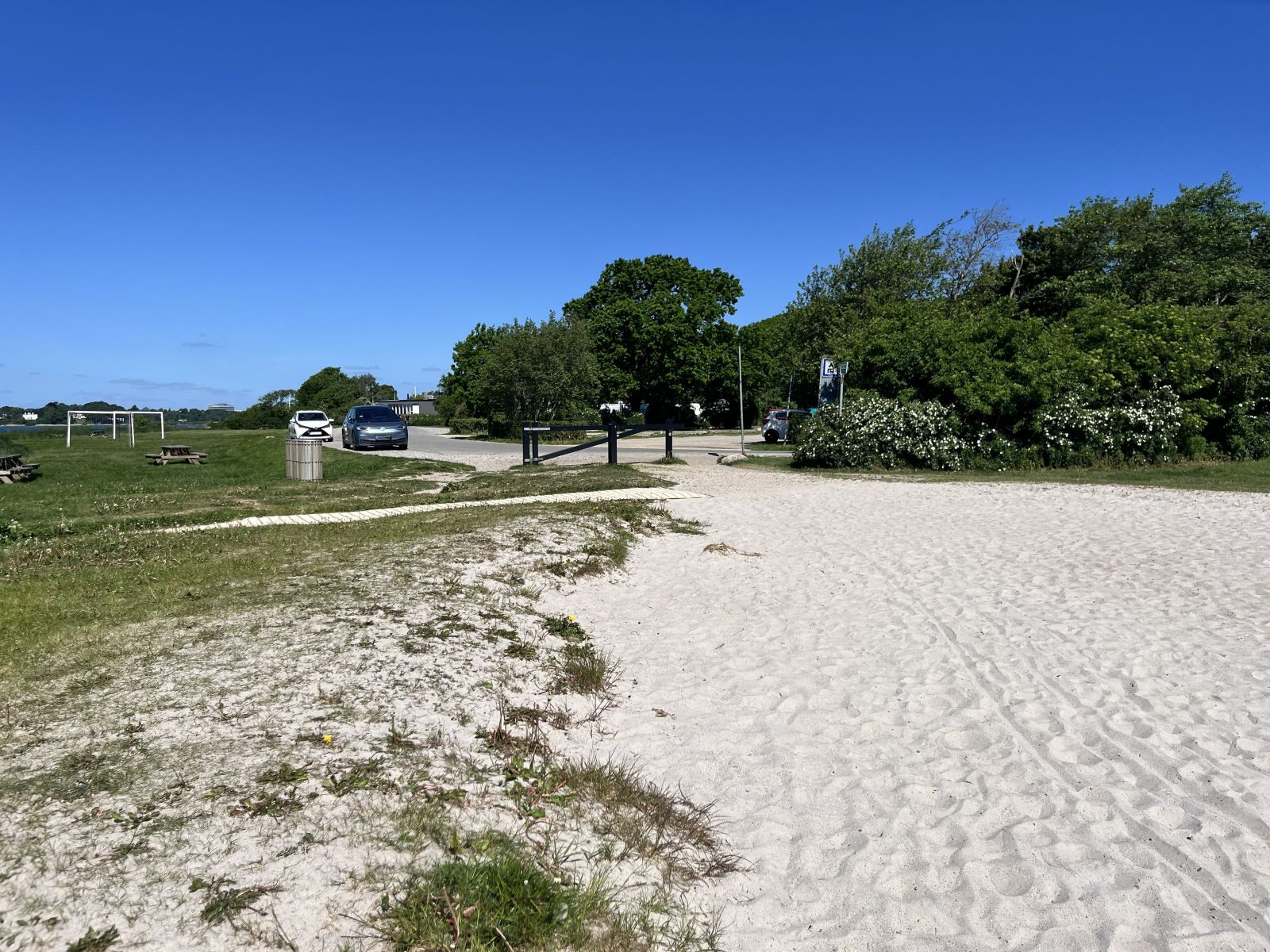 Indgangen til stranden fra den flisebelagte vej. Der er bom for men god plads i siderne til passage. Handikaprampen ses i venstre side af billedet.