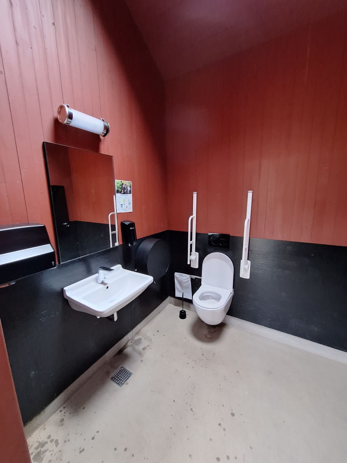 Til venstre for indgangen hænger håndvask med vægmonteret sæbedispenser til højre for håndvasken. Over håndvasken hænger spejl samt lampe. For enden forefindes handicaptoilettet med armlæn og væghængt toiletpapir til højre for brugeren.  Toiletfacilitens