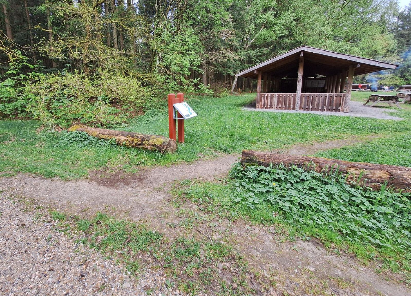 Madpakkehuset set fra Jagtjunkervej. Velkomst tavle ved indgangen af stien der leder fra skovvejen og ind på pladsen