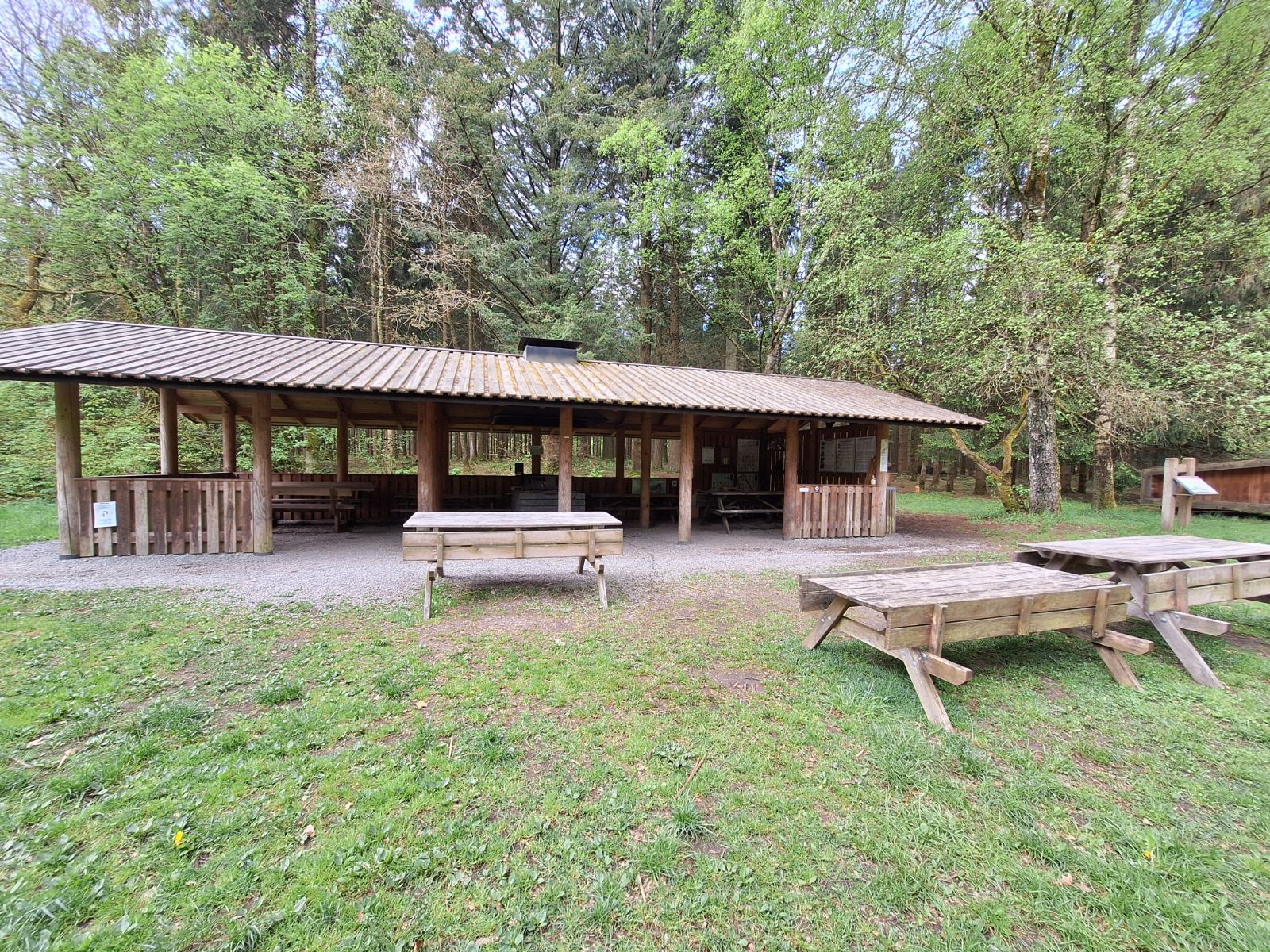 Madpakkehuset set fra langsiden med tre bordebænkesæt foran og shelter set i baggrunden til højre