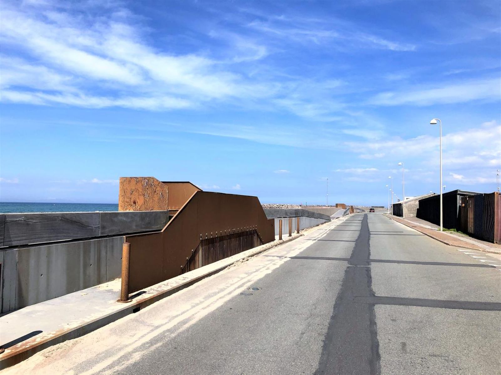 Nede langs Hirtshals Havn hvor man har udsigt til både strand og havet. Underlaget er fortovsfliser og asfalt. 