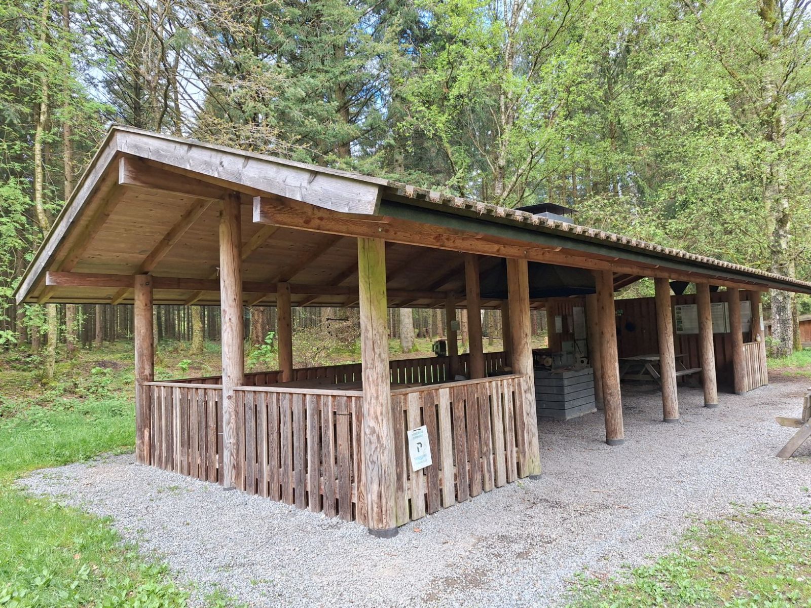 Madpakkehuset set fra indgangen til pladsen. Stampet grus omkring madpakkehuset cirka 1 meter i bredden såvel som stampet grus som underlag inde i.