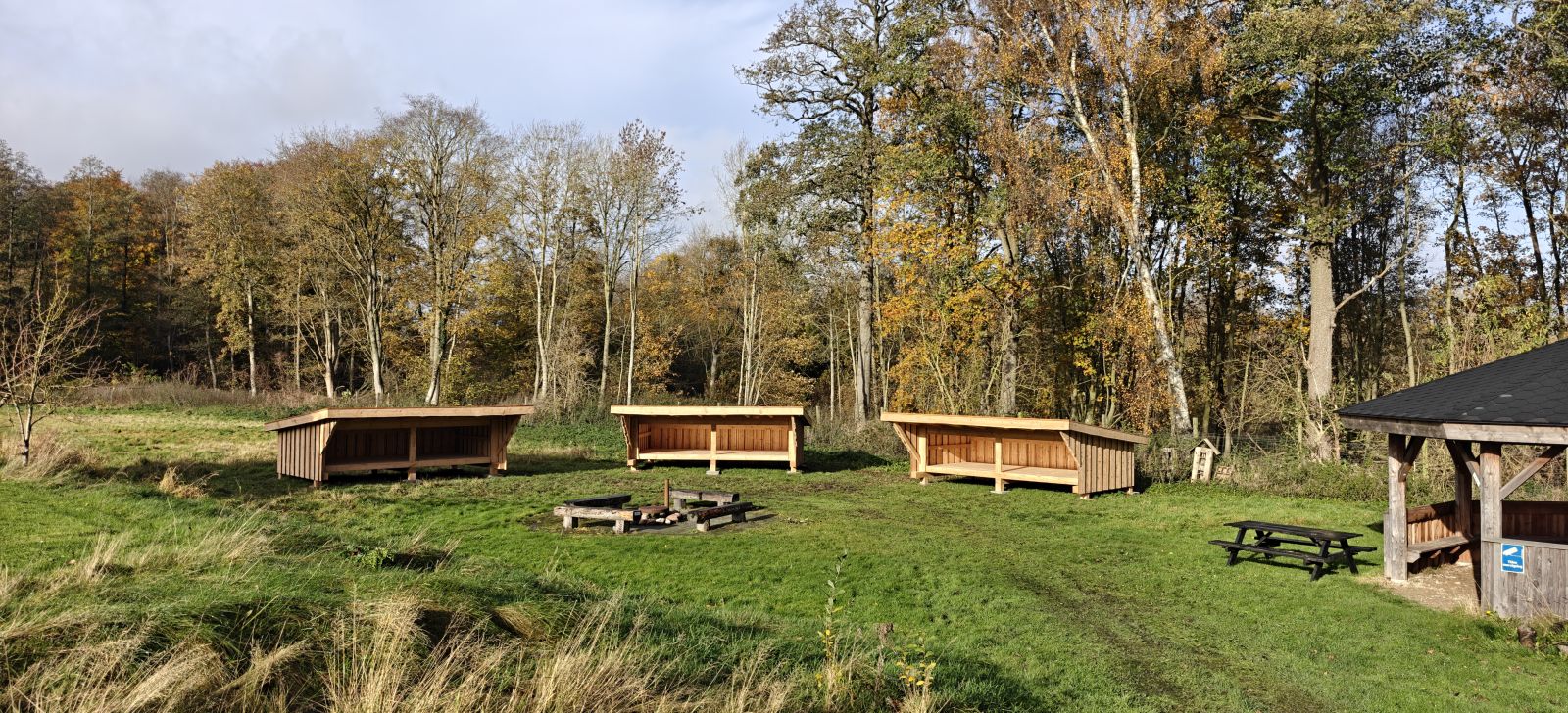Billede viser shelter pladsen med de 3 shelters og bålpladsen i front. Bagved ses skoven.