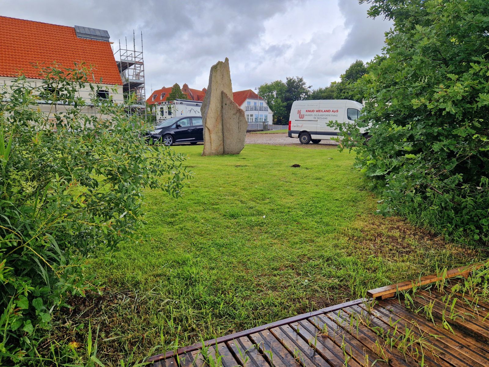 Kig fra fiskeplatformen hen over slået græsstykke til parkeringspladsen