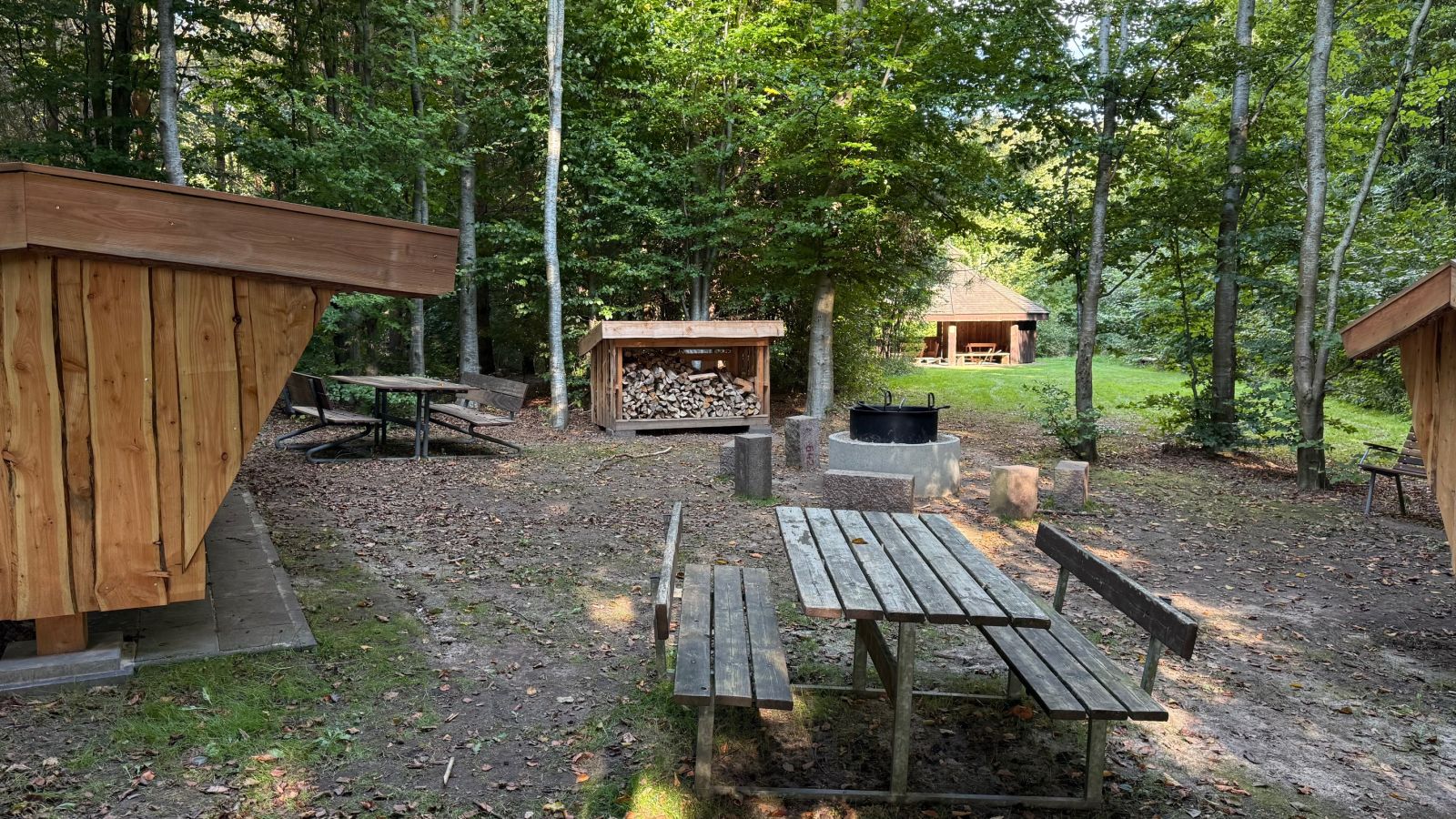 Bålpladsen med grillarrangement foran shelterne, madpakkehuset i baggrunden