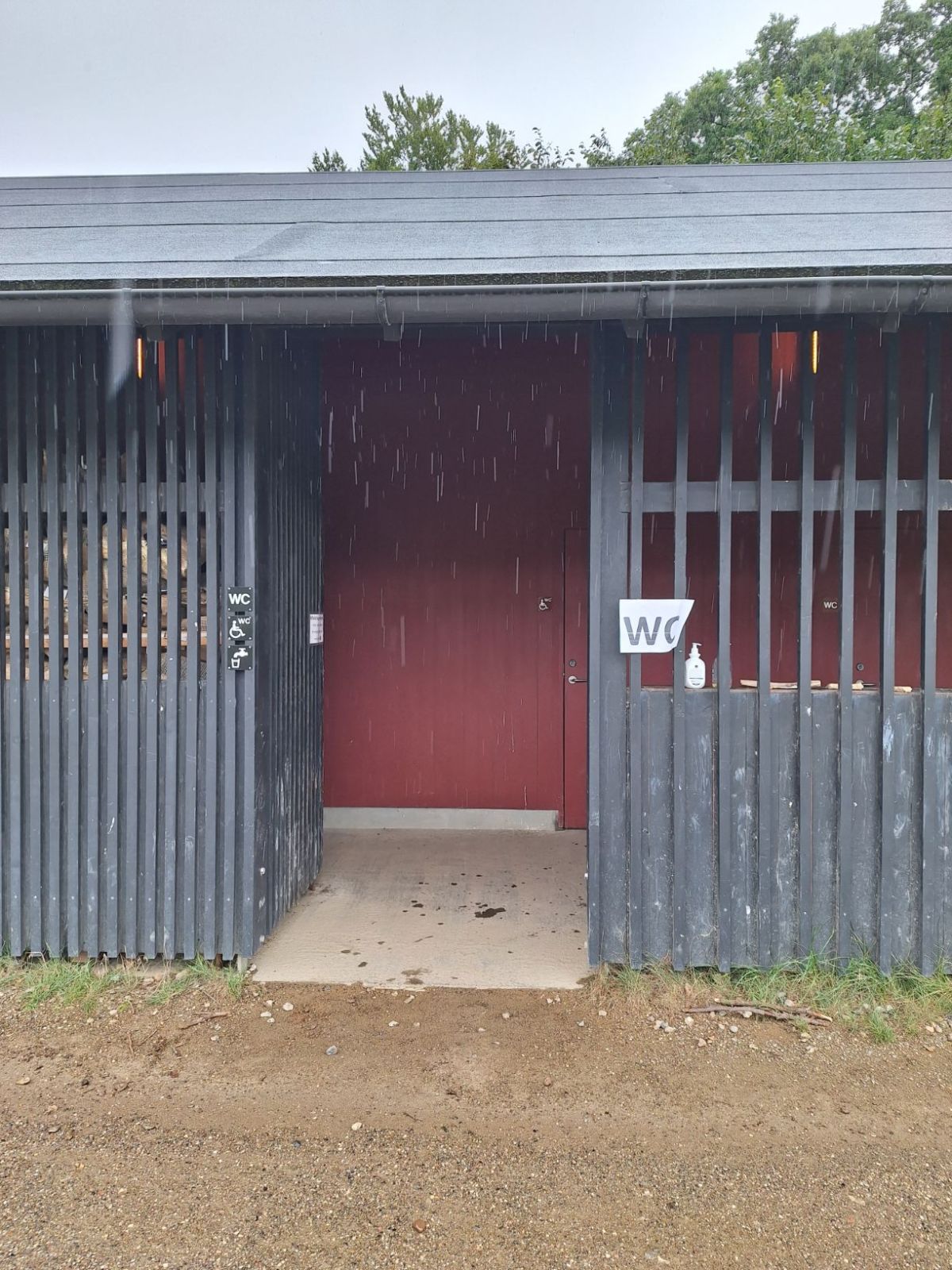 Indgang til toiletterne fra midten af laden. Toiletterne findes til højre fra indgangen med handicaptoilettet først for. Overgangen fra stampet grussti til gulv er jævn. 