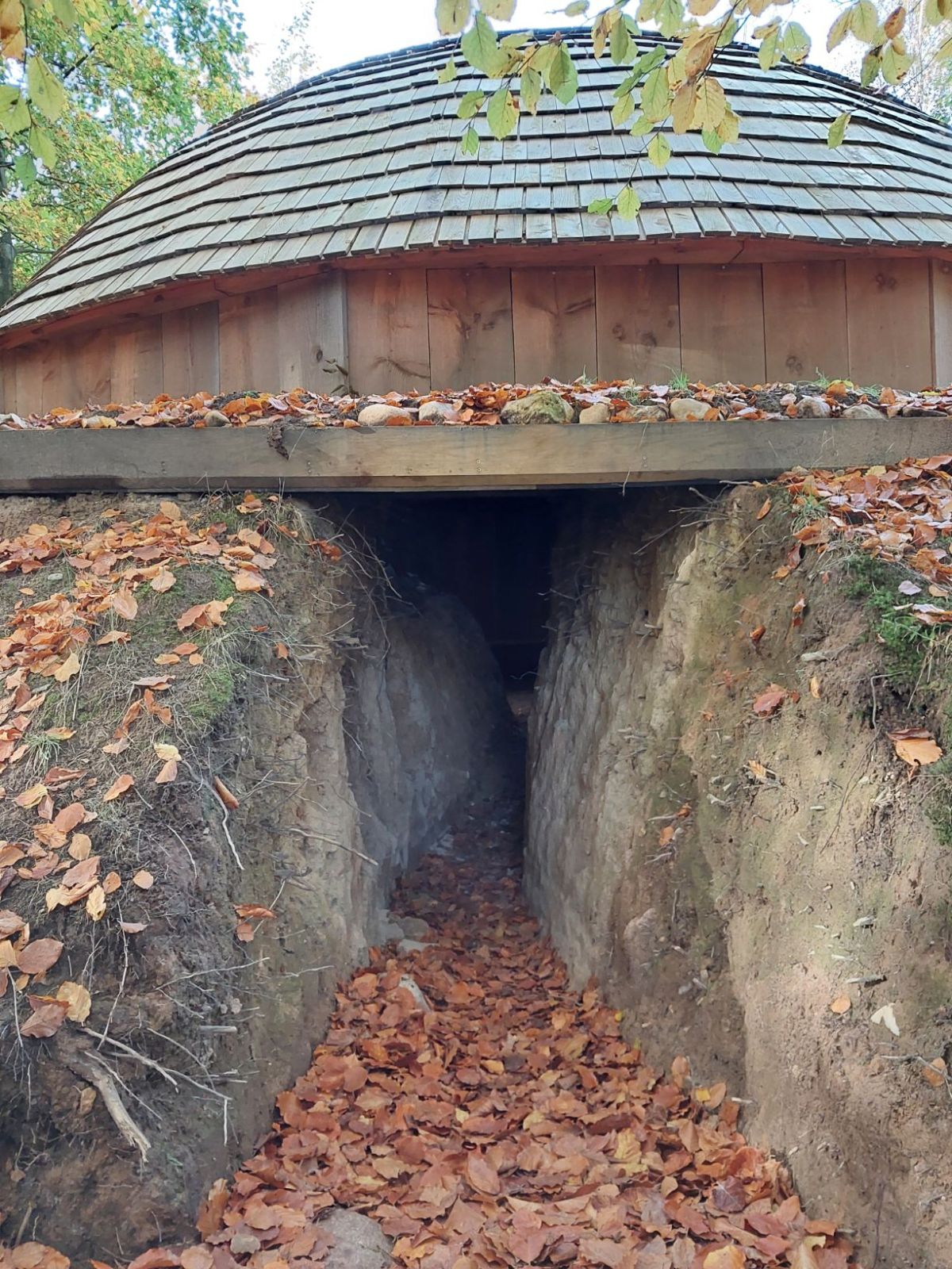 Åbningen ind til jordhuset sker ind i en skrænt med jord på begge sider og trætag for oven.