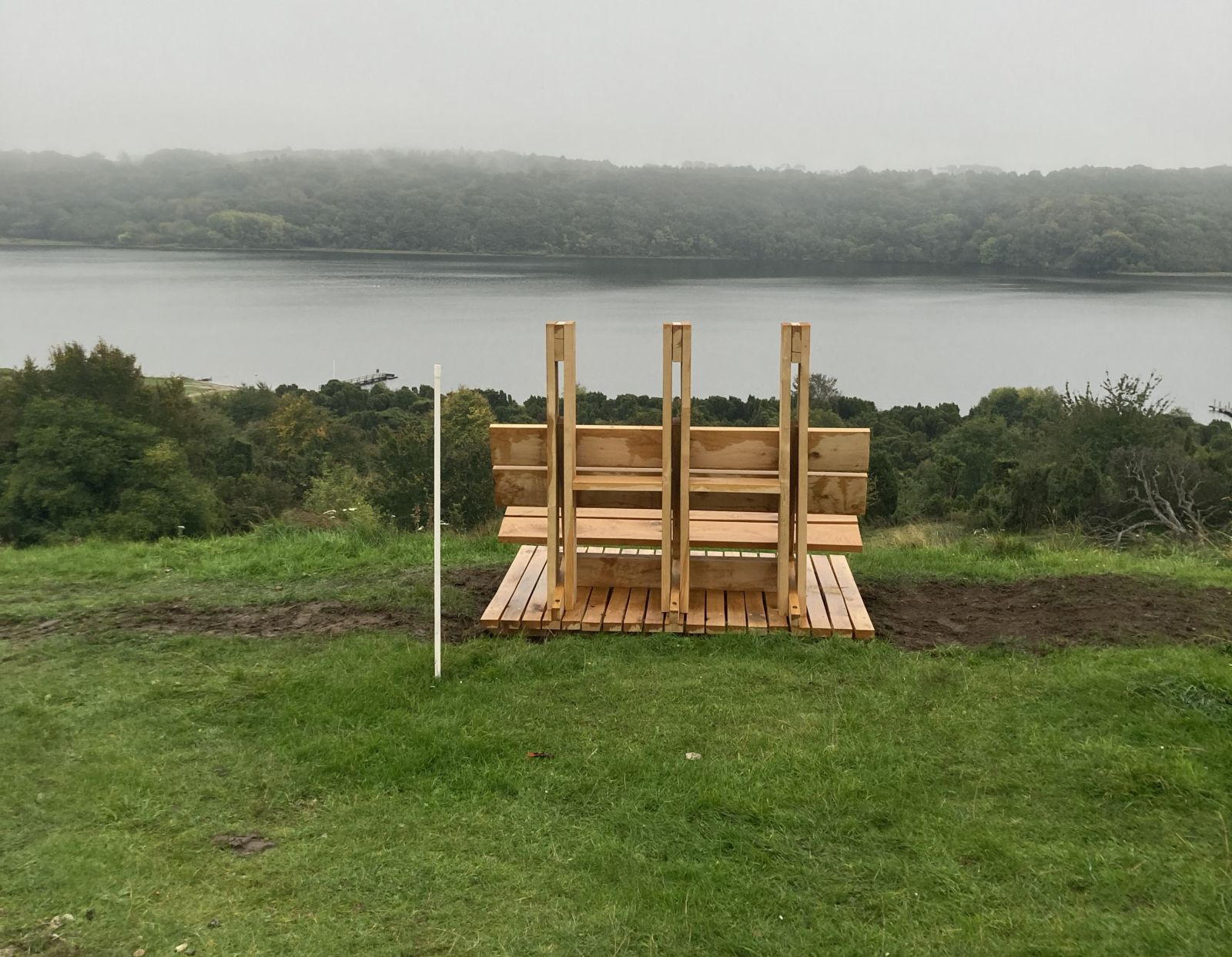 Markant bænk med tre søjler set bagfra placeret med udsigt over Mariager Fjord