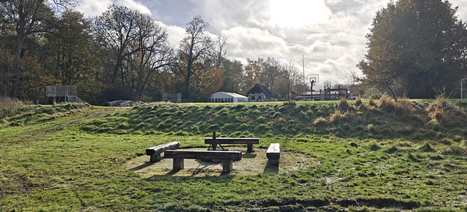 Billede viser bålpladsen med 4 bænke på en græsplæne med en lille vold bagved