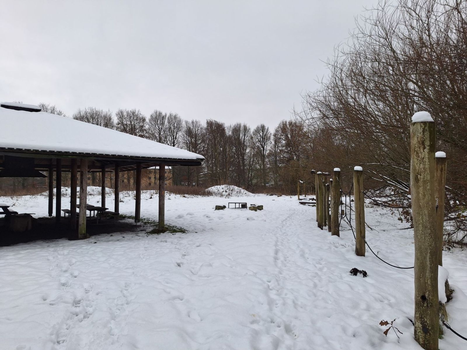 Vinterbillede af bålhytten med tarzanbane til højre for og et mindre bålsted under åben himmel for enden af bålhytten