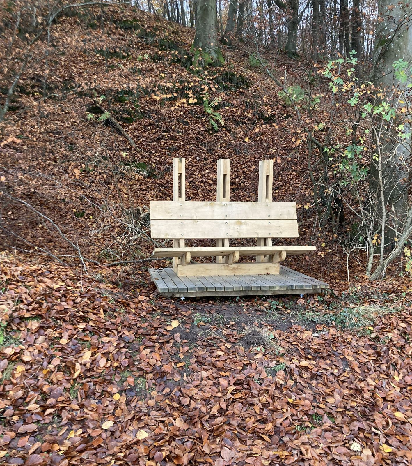 Markant bænk med tre søjler set forfra placeret op ad skoven
