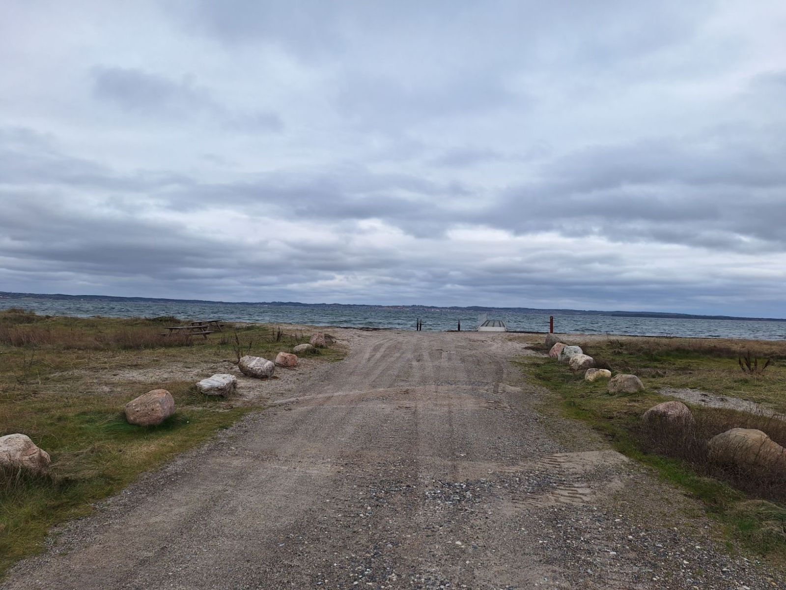 Efter parkeringspladsen kan man følge grusvejen ned til vandet. Vejen er indrammet af store sten på begge sider.