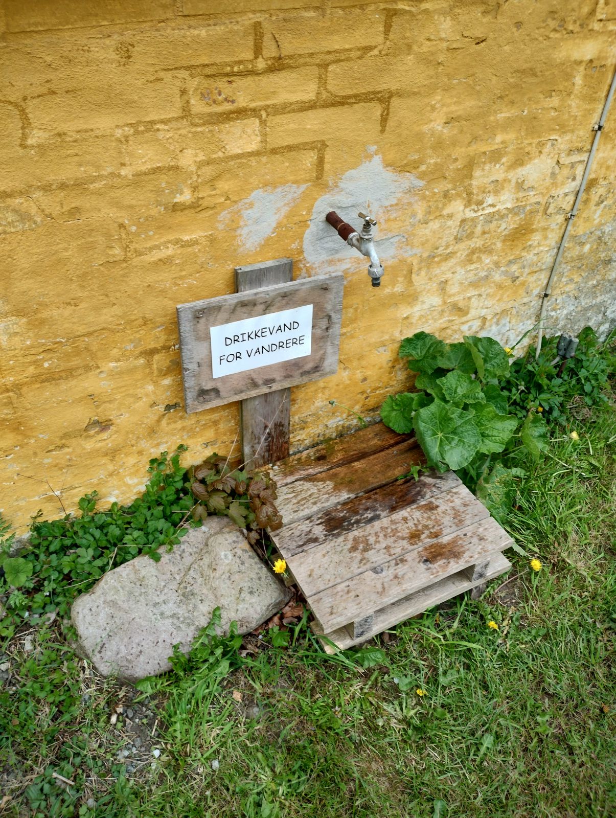 Vandpost på gul muret gavl.