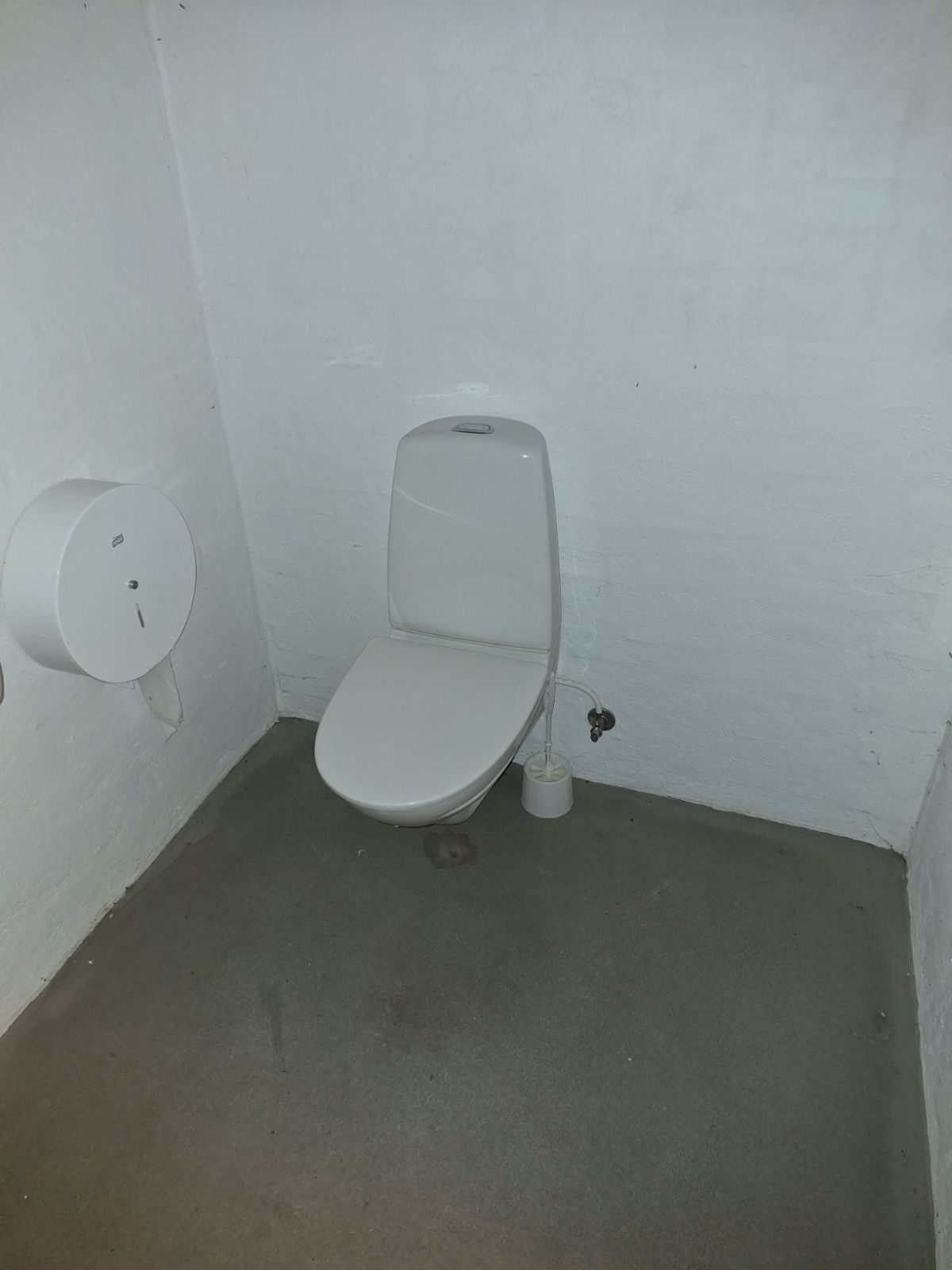 Toilet med væghængt toiletpapirsholder mod venstre.