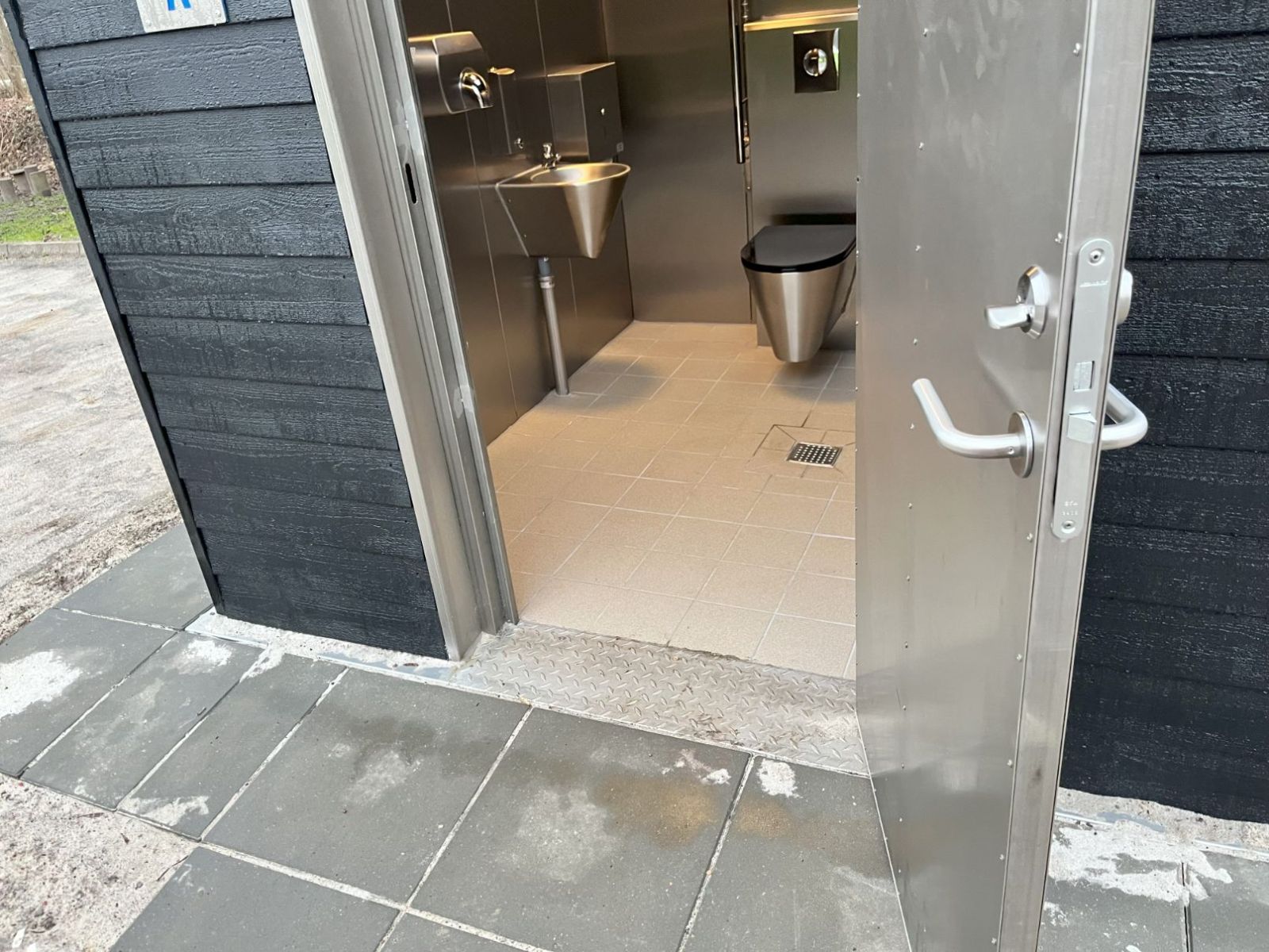 Adgangen til toilettet er via en flisebelagt sti med svag hældning og uden dørtrin.