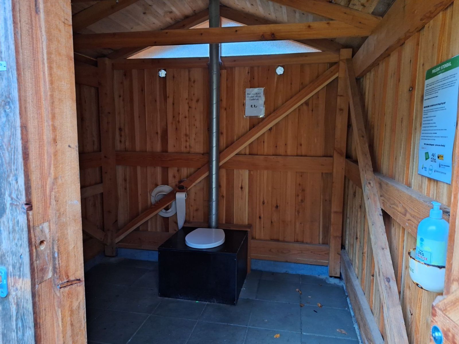 Billede af toilettet fra døren med sæbe hængende til højre for indgangen. Ekstra børnesæde til toilettet hænger på væggen ved toilettet.