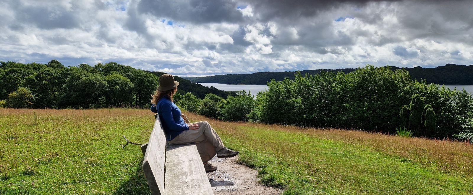 Lang bænk i massiv bænk placeret på toppen af en bakke med udsigt udover Mariager Fjord.