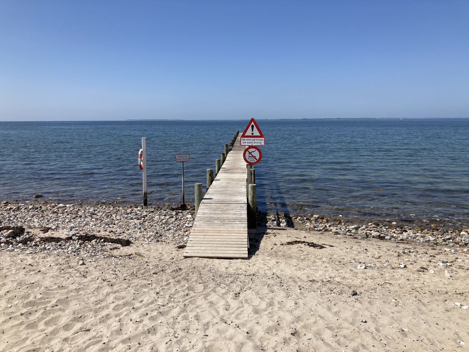 Adgangen til badebroen går over sandstranden. Der er et mindre trin fra stranden til broen.